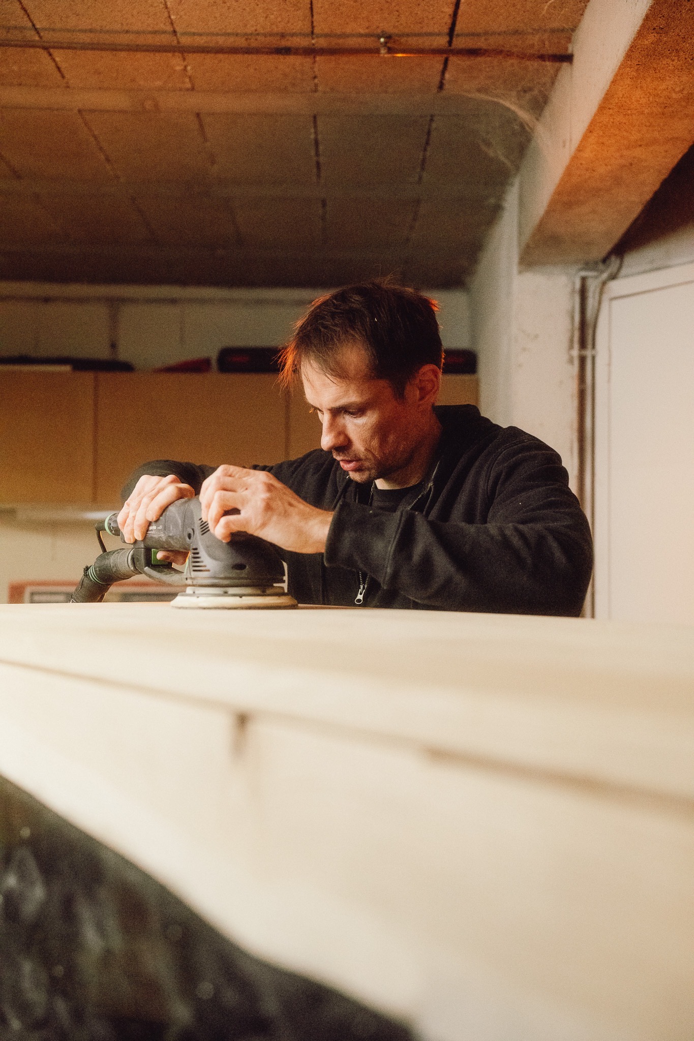 Xavier ponçant un plateau de bois dans son atelier